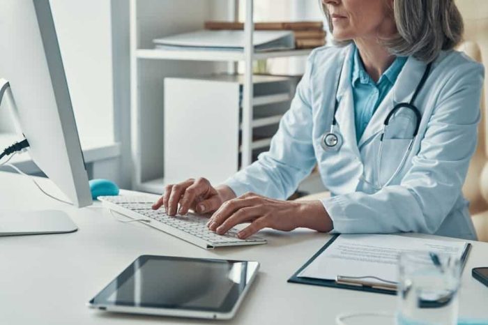 Close up of female doctor in white lab coat working using computer while sitting in her office